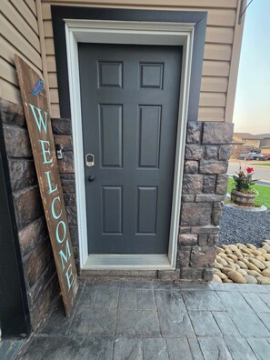 A dark grey door with a welcome sign, a stone wall, and a stone pathway leading to the entrance.