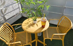 Een klein rond tafeltje met twee gele stoelen, een plastic beker met rietje en een kleine potplant op tafel.