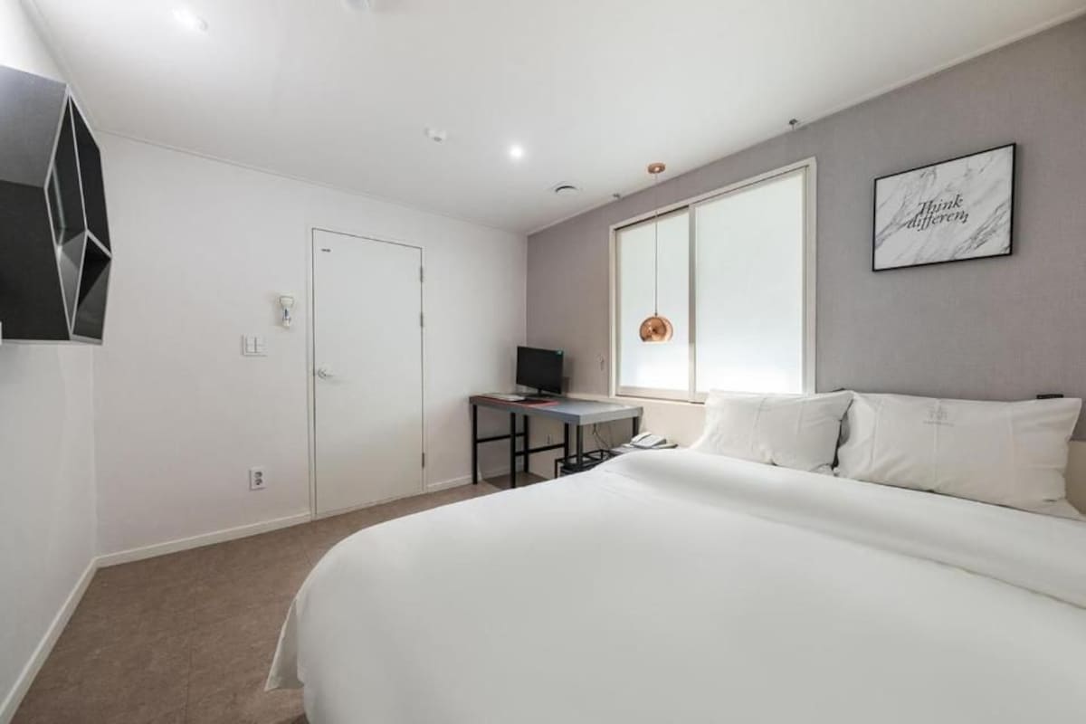 A bedroom with a bed, a desk, a television, and a window.