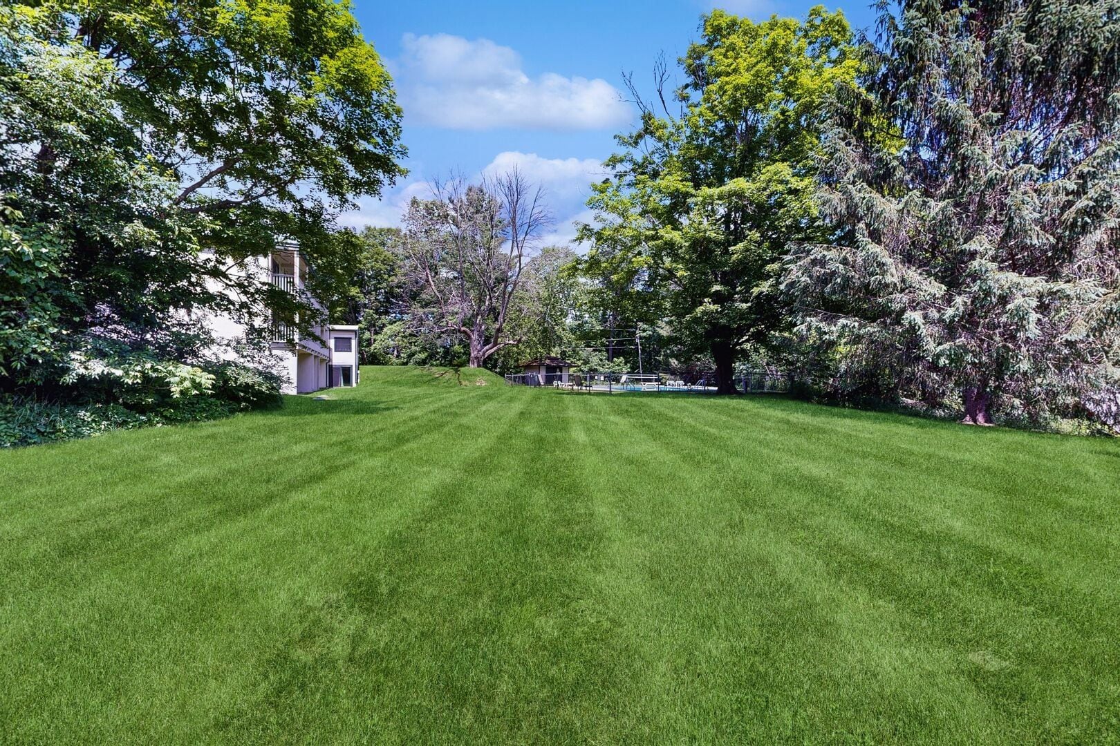 A well-maintained lawn with a small building, surrounded by trees and a clear sky.