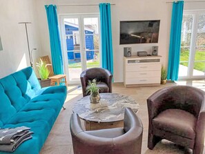 A living room with a sofa, two armchairs, a coffee table, a TV, and a sliding glass door leading to a balcony. - Mermaid by Interhome (Seebad Altefähr)