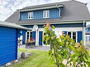A two-story house with a blue exterior, a satellite dish, and a garden with plants and a lawn. - Mermaid by Interhome (Seebad Altefähr)