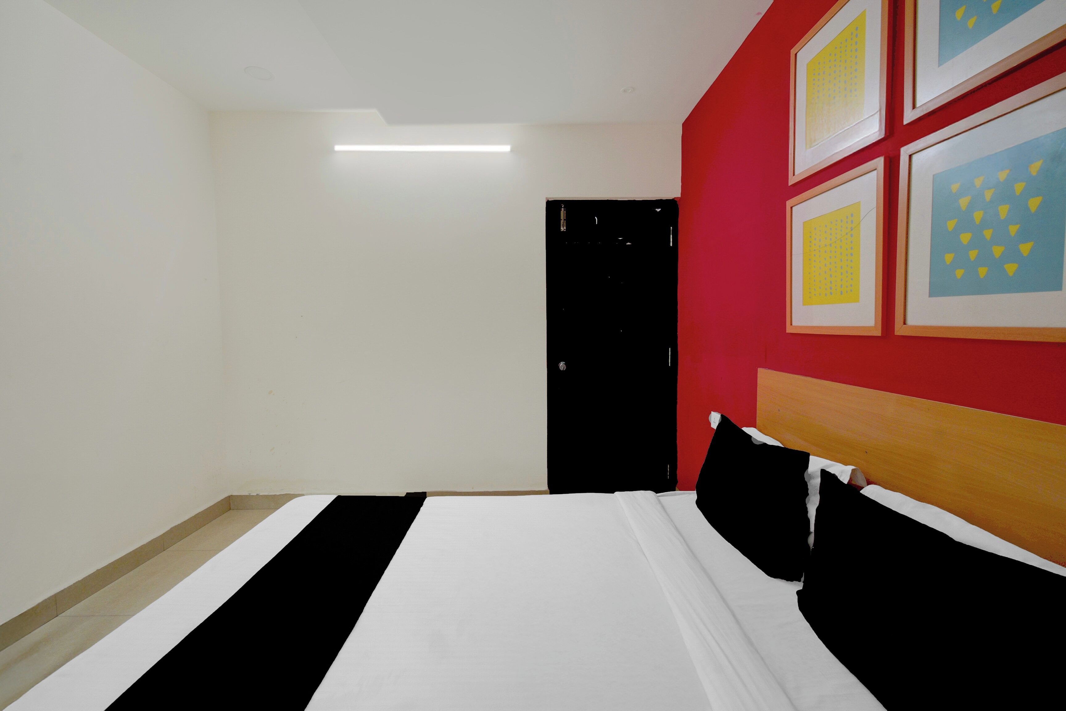 A hotel room with a bed, a door, and a wall with framed pictures.