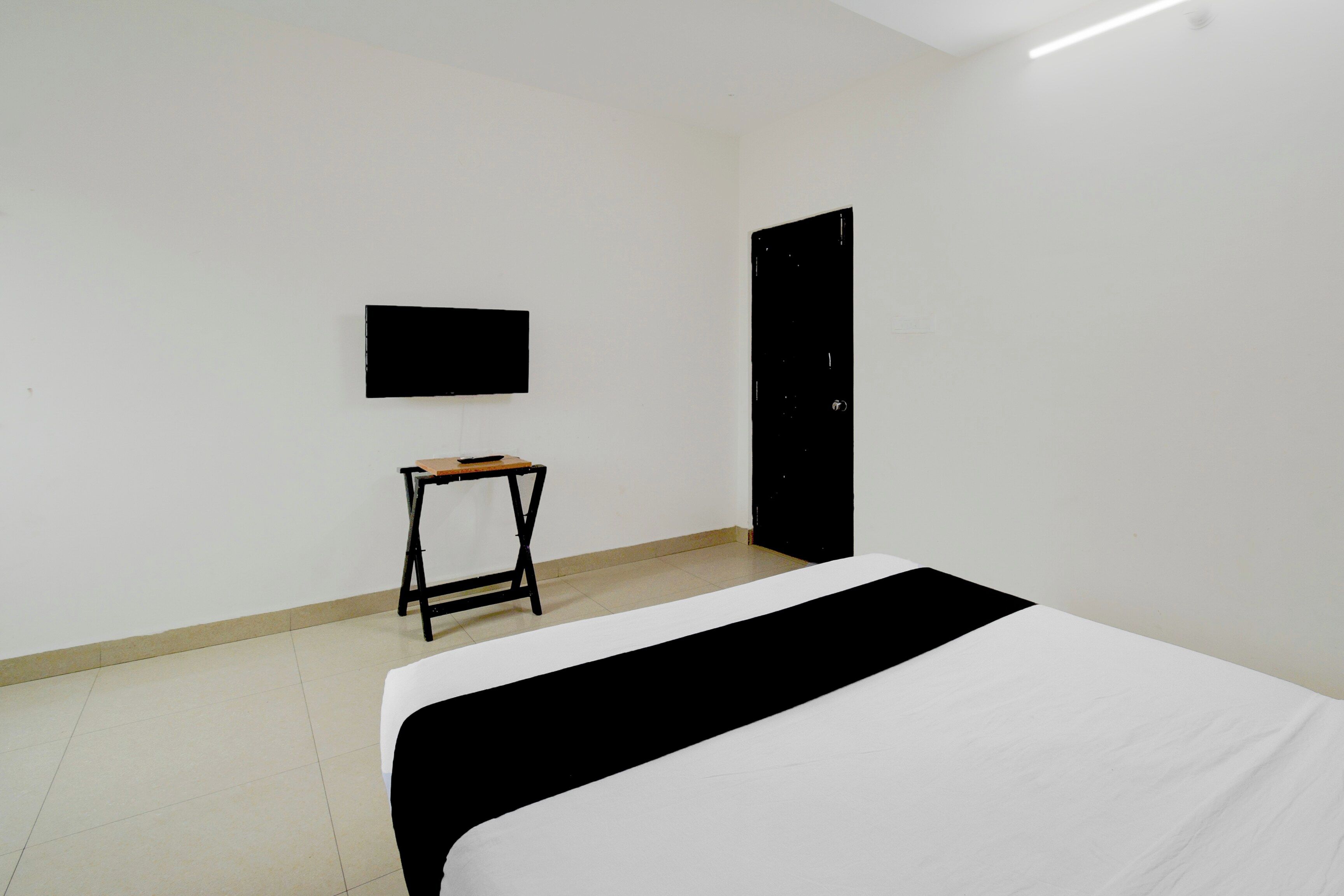 A room with a bed, a small table, a wall-mounted TV, and a door.