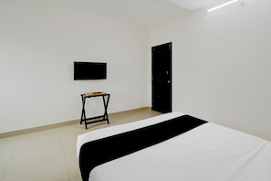 Una habitación con una cama, una mesita, un televisor instalado en la pared y una puerta.