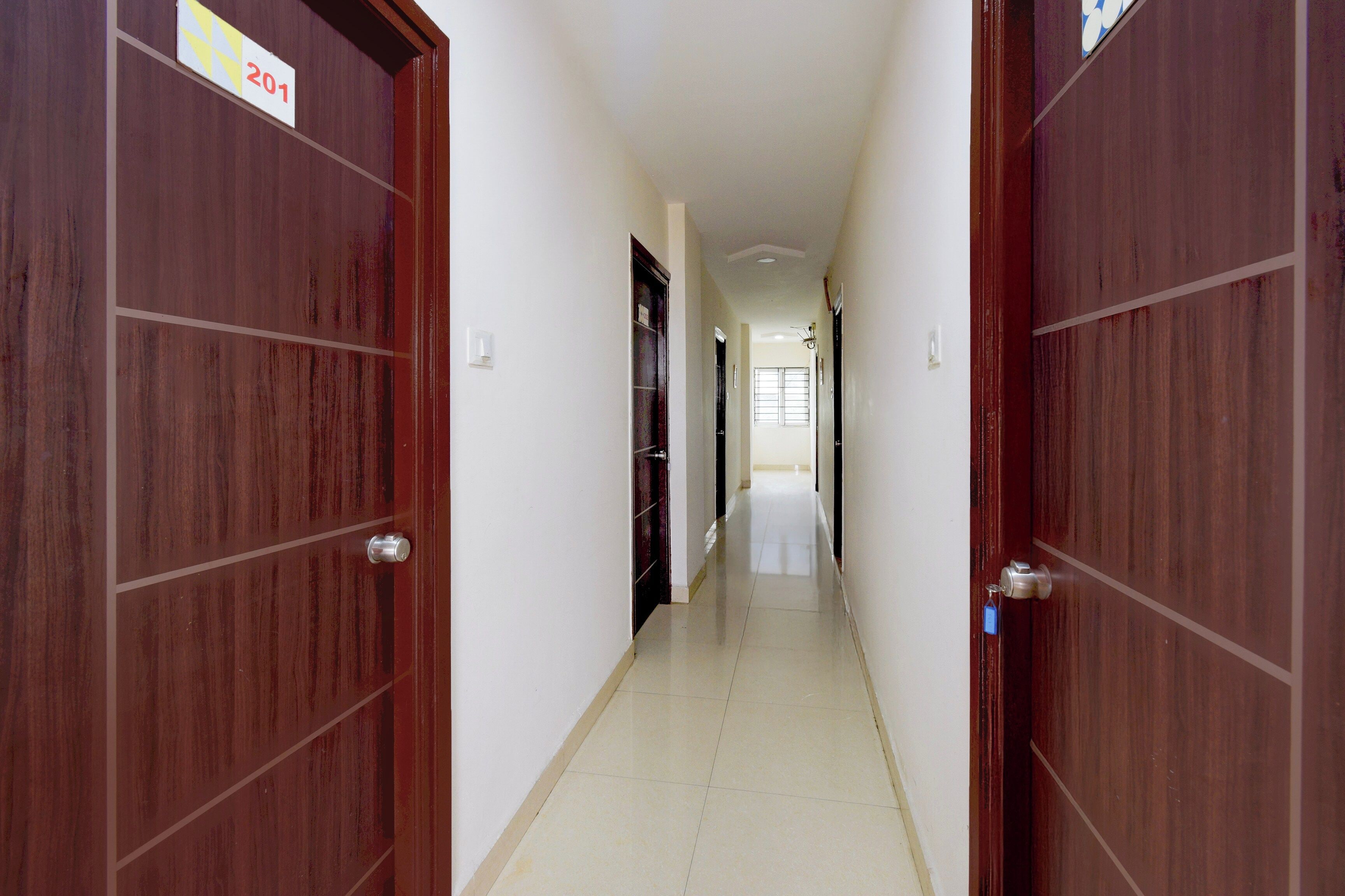 A corridor with wooden doors, a tiled floor, and a light switch on the wall.
