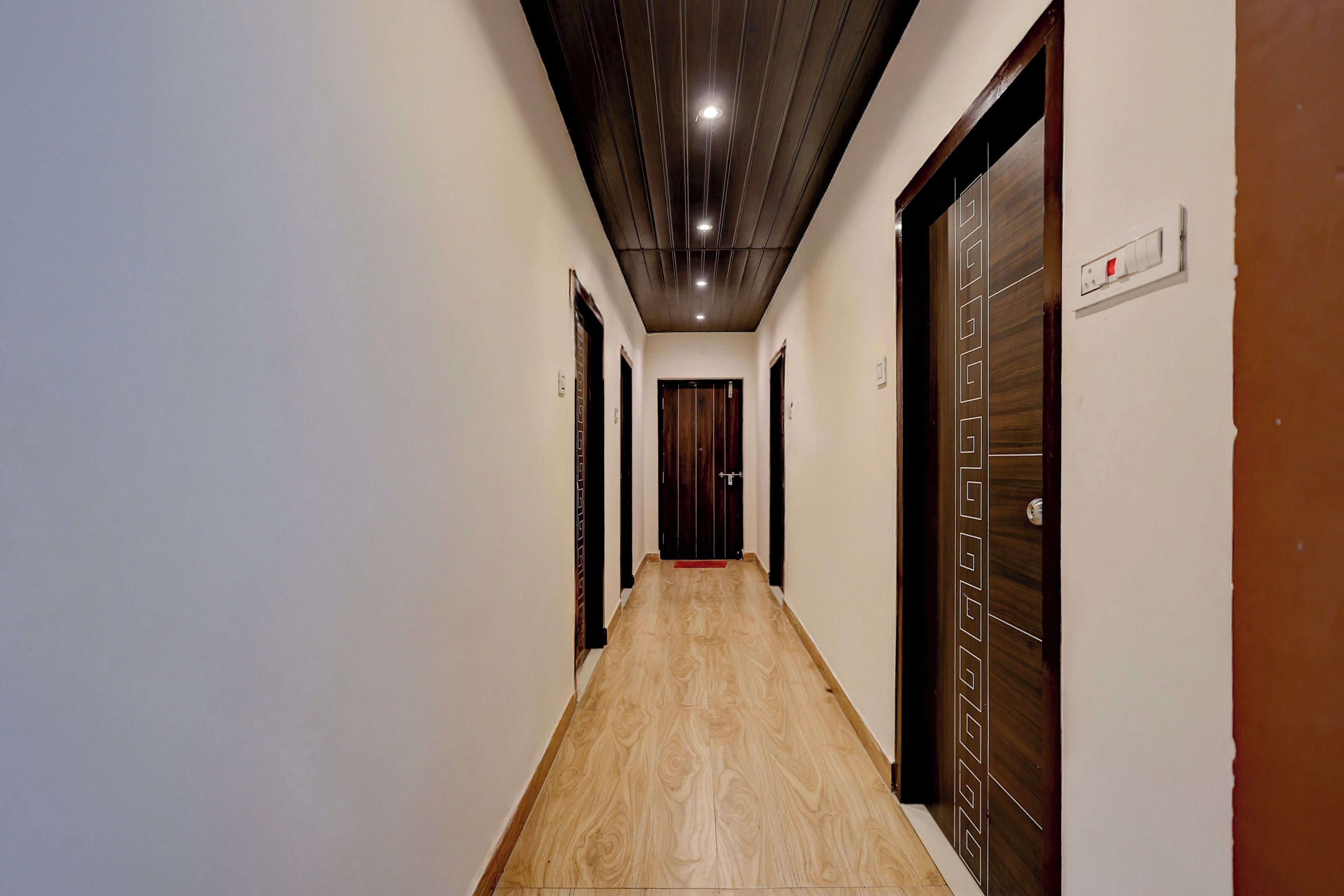 A corridor with wooden flooring, white walls, and doors with geometric patterns.