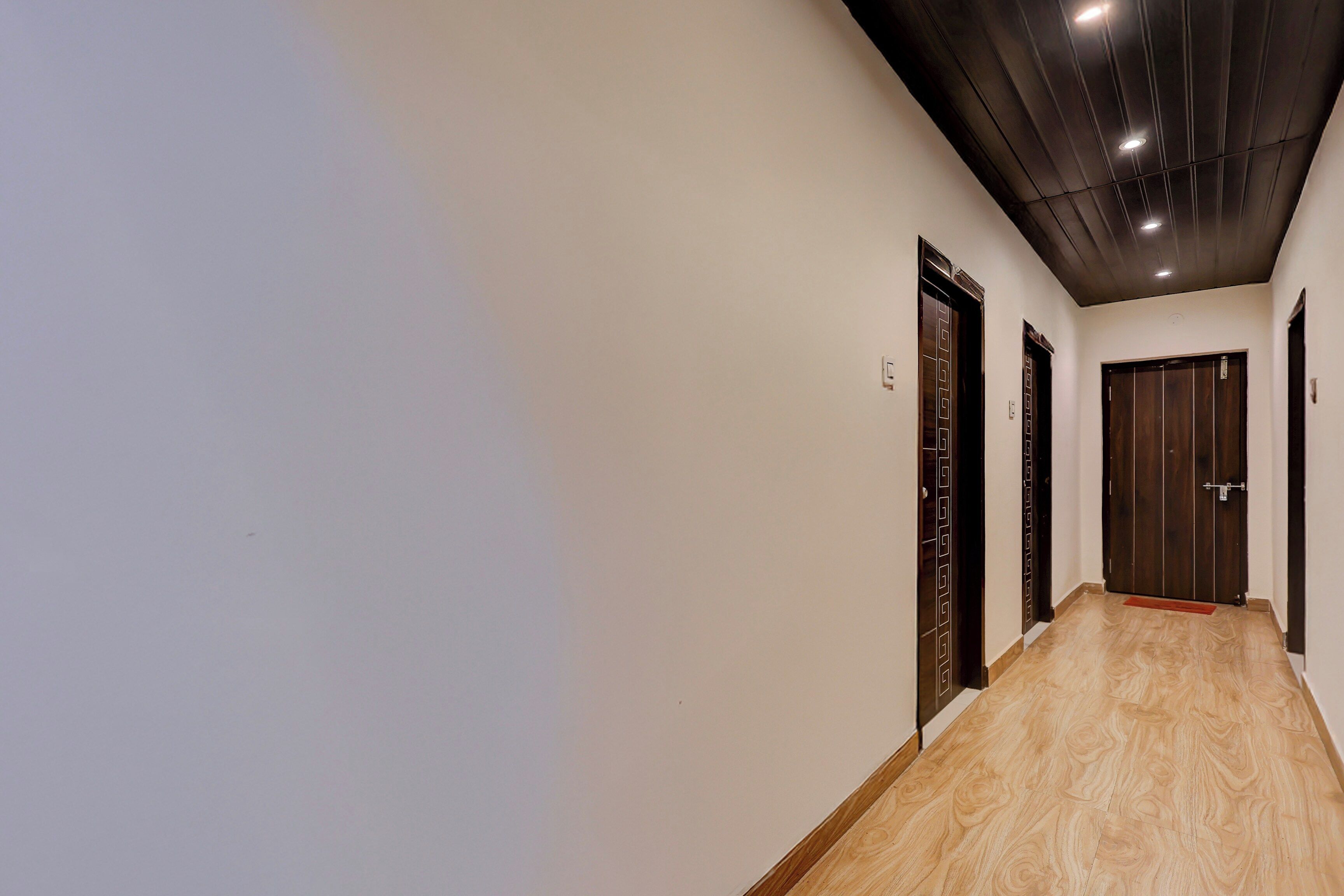 Un pasillo con piso de madera, puertas oscuras de madera e iluminación empotrada en el techo.