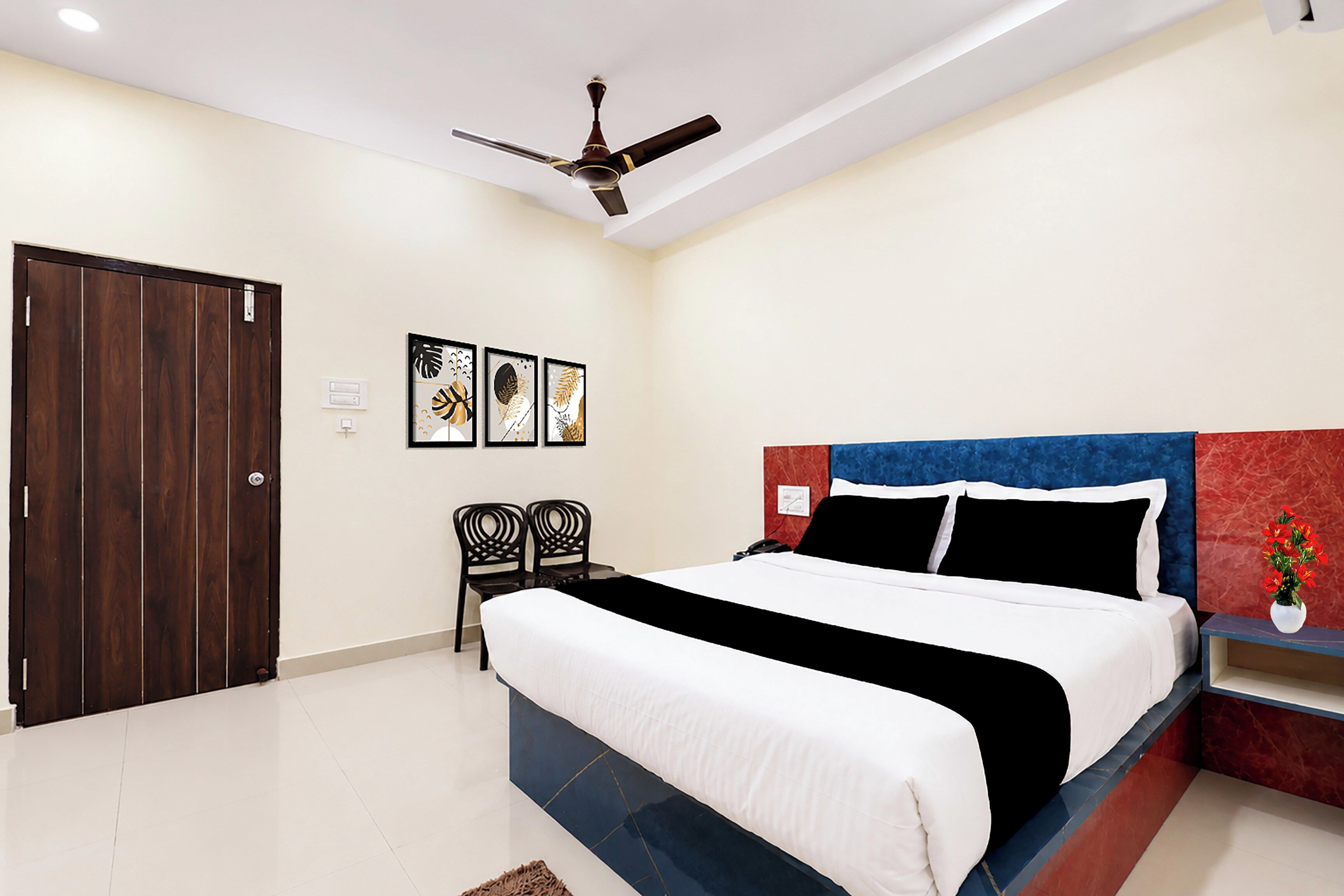 A bedroom with a bed, a ceiling fan, a door, two chairs, and wall art.