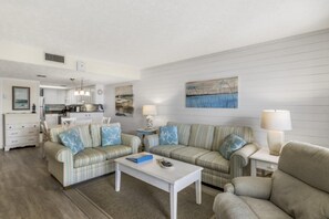A living room with striped sofas, a coffee table, and a dining area with a kitchen in the background. - Tequila Sunrise at Pinnacle Port B1-308 (Panama City Beach)