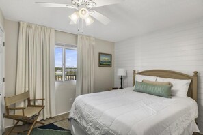 A bedroom with a bed, a chair, a window with curtains, a ceiling fan, and a nightstand with a lamp. - Tequila Sunrise at Pinnacle Port B1-308 (Panama City Beach)