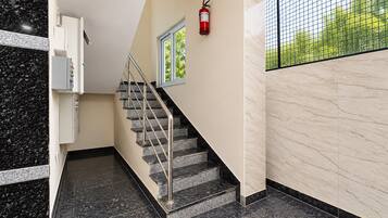 Een trap met een leuning, een brandblusser bevestigd aan de muur, en een raam met uitzicht op groen.