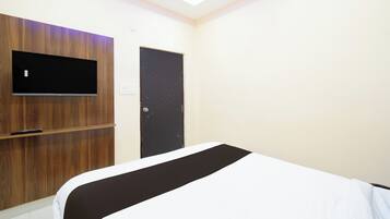 Een slaapkamer met een bed, een aan een houten paneel bevestigde televisie, een deur en een lichtschakelaar aan de muur.