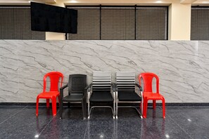 Un'area reception con una parete in marmo, uno schermo nero e quattro sedie dai diversi design.