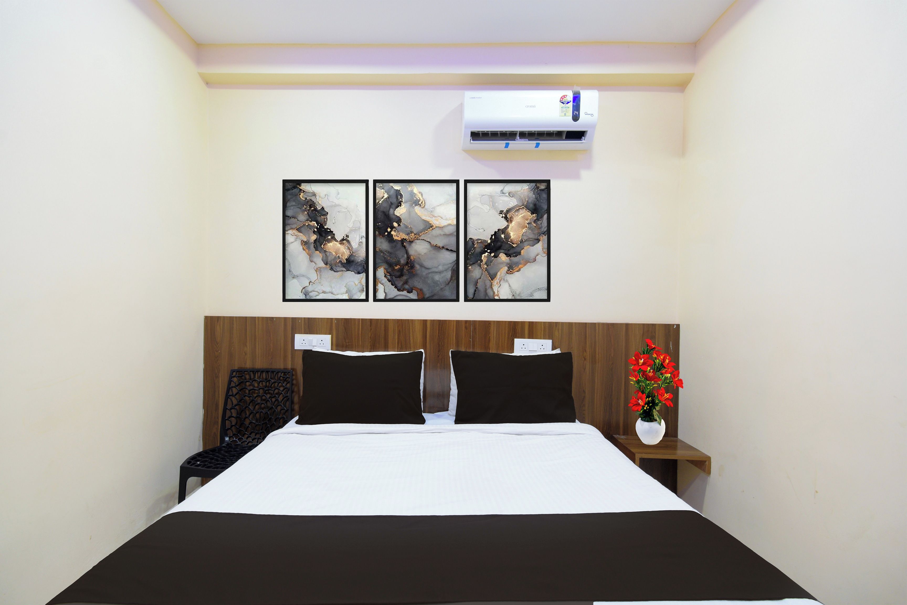 Une chambre d’hôtel avec un lit, une table de chevet ornée d’un vase de fleurs et trois tableaux abstraits accrochés au mur.