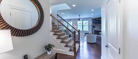 A staircase with wooden railings and a handrail, leading to a living area with a fireplace and a stone wall.