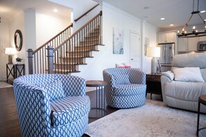A modern living room with a staircase, a dining area, and a kitchen. - 3BR home in Reynolds Landing with patio, grill & foosball (Greensboro)
