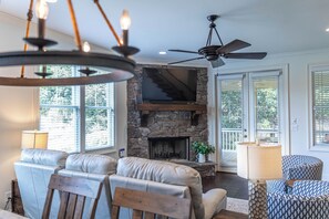 A living room with a stone fireplace, leather sofas, a ceiling fan, and large windows. - 3BR home in Reynolds Landing with patio, grill & foosball (Greensboro)