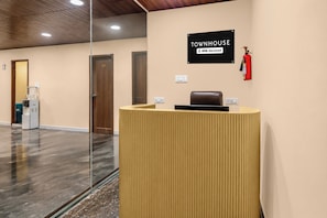 Una mesa de recepción con un cartel que indica que es atendida por OYO, un área de recepción con un extintor y un dispensador de agua.