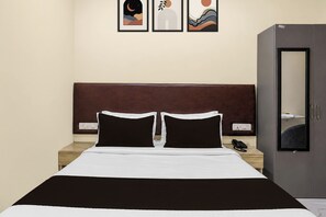 Una cama individual con colcha blanca y negra, dos almohadas negras, una mesita de noche de madera con un teléfono y un armario gris.