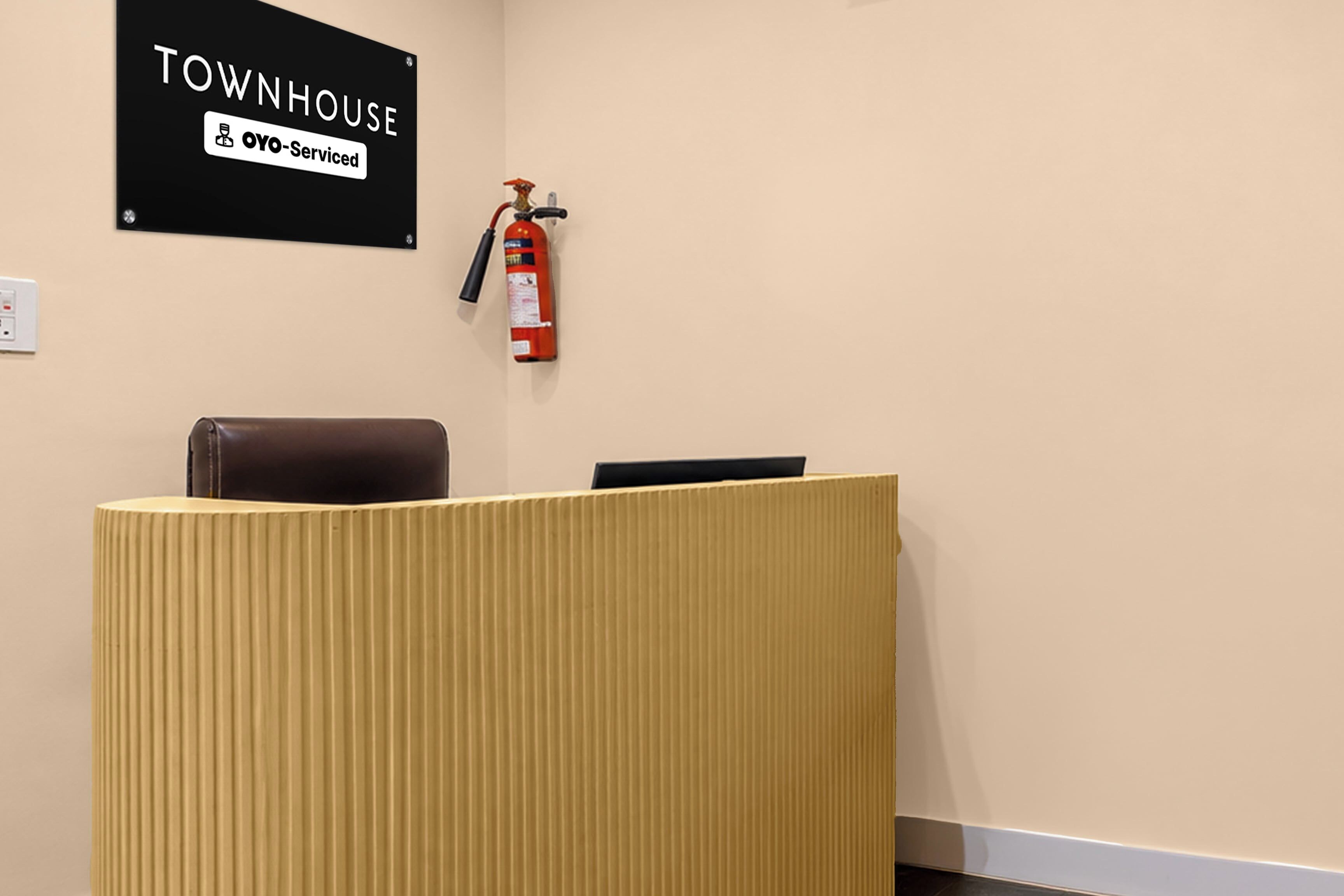 Un comptoir d’accueil avec une enseigne indiquant « TOWNHOUSE OYO – Services hôteliers » et un extincteur fixé au mur.