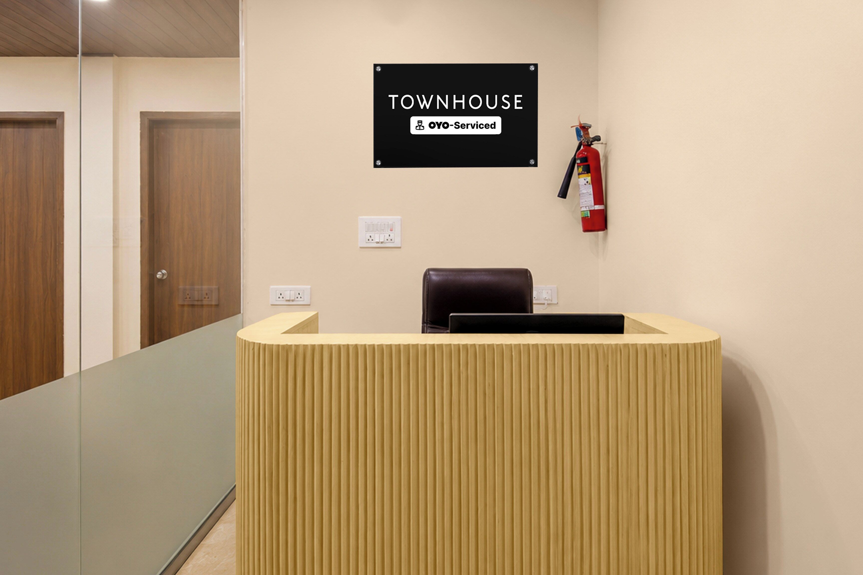 A reception desk with a sign above it that reads 'TOWNHOUSE YOYO-Serviced.' There is a fire extinguisher mounted on the wall to the right of the desk.