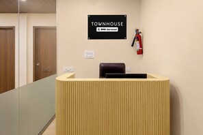 Un mostrador de recepción con un cartel encima que dice 'TOWNHOUSE YOYO-Serviced'. Hay un extintor de incendios montado en la pared a la derecha del mostrador.