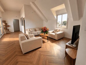 A spacious living room with a herringbone wooden floor, a sectional sofa, a small coffee table, and a television. - Elegance in the Heart of the Golden Square (Saint-Denis)