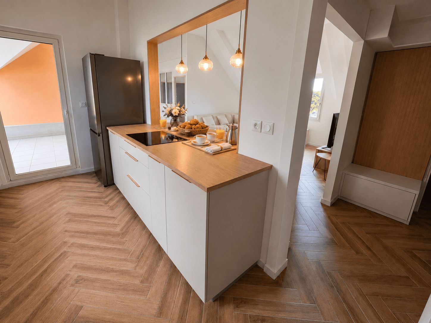 A modern kitchen with a built-in island, a refrigerator, pendant lights, and a view to a balcony.