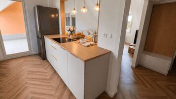 A modern kitchen with a built-in island, a refrigerator, pendant lights, and a view to a balcony.