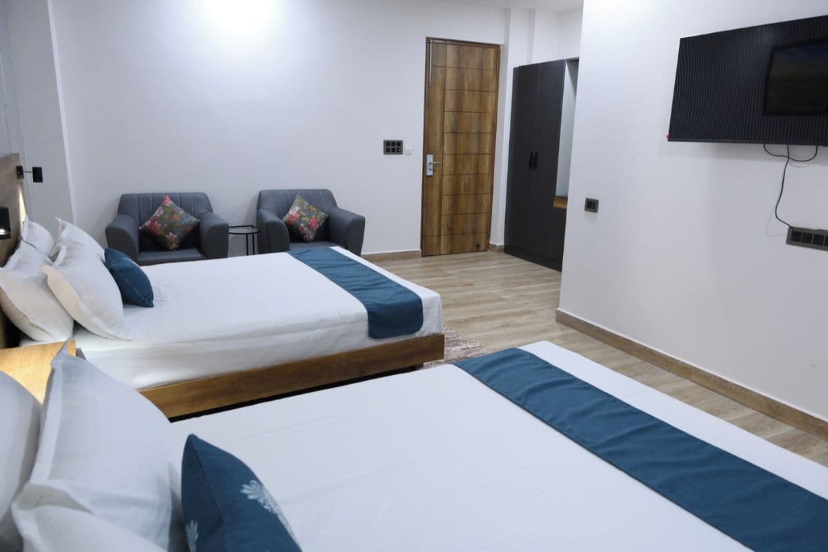 Una camera d'albergo con due letti, una TV montata a parete, una porta in legno e un tavolino con sedie.