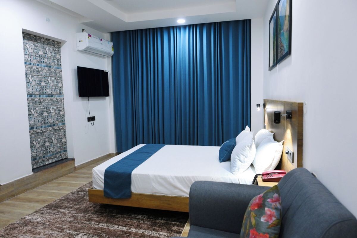 Un dormitorio con cama, televisor, aire acondicionado instalado en la pared, una ventana con cortinas azules y un sofá.