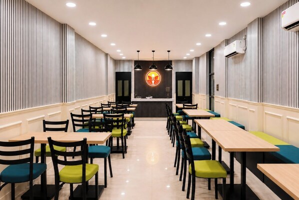 A restaurant with a central counter, multiple tables, and chairs. - Sama Inn (Rishikesh)