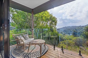 Ein Balkon mit einem Korbsessel und einem runden Tisch, mit Blick auf eine üppige Landschaft.