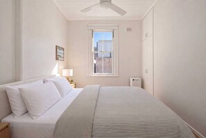 Une chambre à coucher avec un lit, une table de chevet, une fenêtre et un ventilateur de plafond.