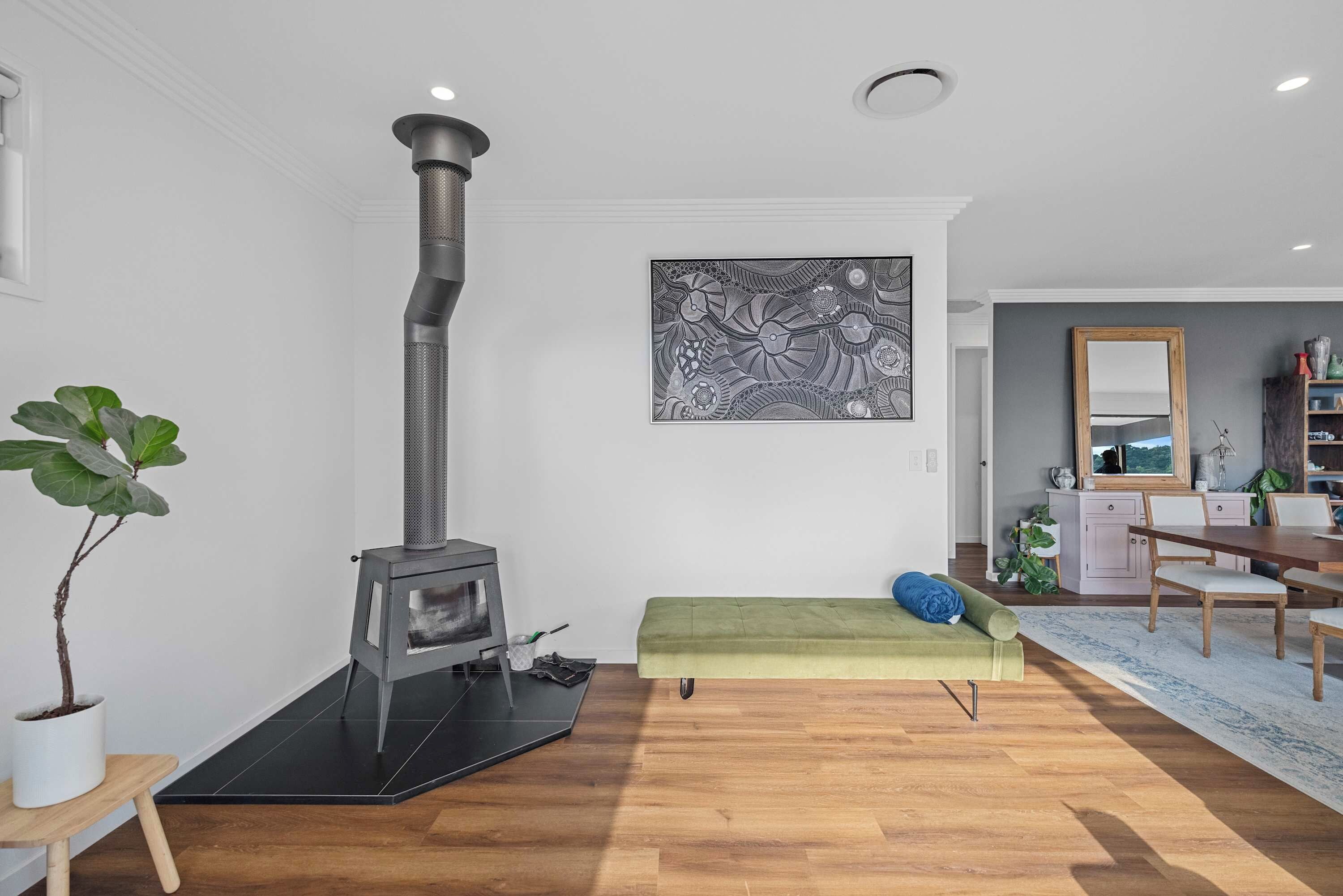 Ein modernes Wohnzimmer mit Kaminofen, einem grünen Sofa, einem Essbereich und einem großen abstrakten Gemälde an der Wand.