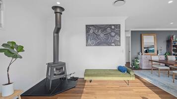 Ein modernes Wohnzimmer mit Kaminofen, einem grünen Sofa, einem Essbereich und einem großen abstrakten Gemälde an der Wand.