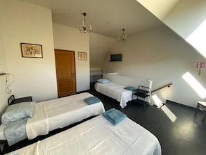 A room with two single beds, a desk, a chair, a TV mounted on the wall, and a chandelier. - Ferme du Laid Burniat (Chaumont-Gistoux)