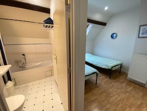 A bathroom with a bathtub and a toilet, a bedroom with a bed and a radiator, and a hallway with a door leading to the bathroom. - Ferme du Laid Burniat (Chaumont-Gistoux)