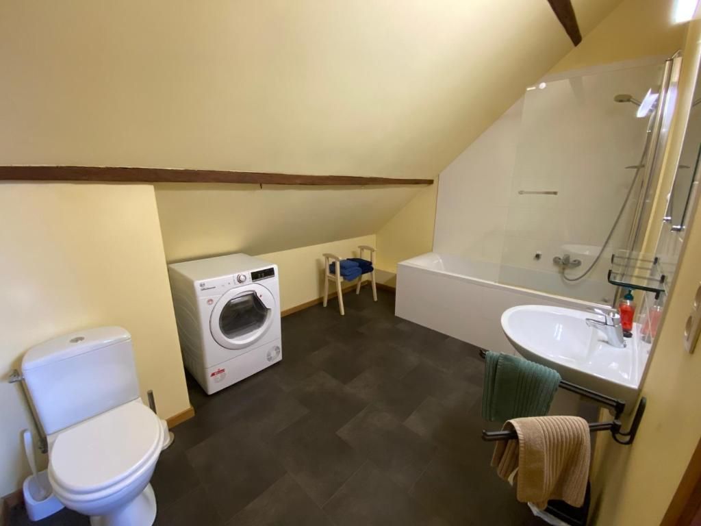 Een badkamer met toilet, wasmachine en bad.