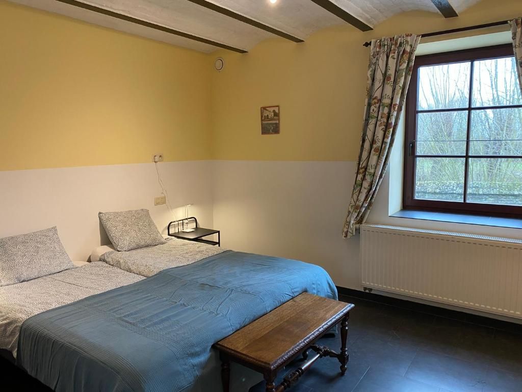 Una camera da letto con due letti, una panca, una finestra con tende e un termosifone.