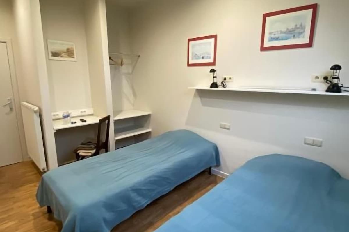 A room with two single beds, a desk, and a chair.