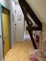 Un pasillo con piso de madera, una puerta amarilla y una escalera junto a un muro de ladrillo.