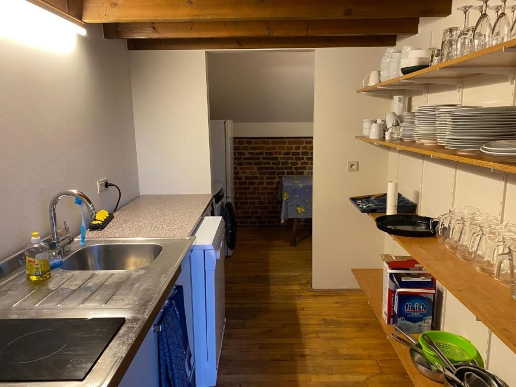 A kitchen with a sink, dishwasher, and wooden shelves with dishes and glasses.