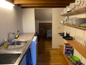 A kitchen with a sink, dishwasher, and wooden shelves with dishes and glasses.