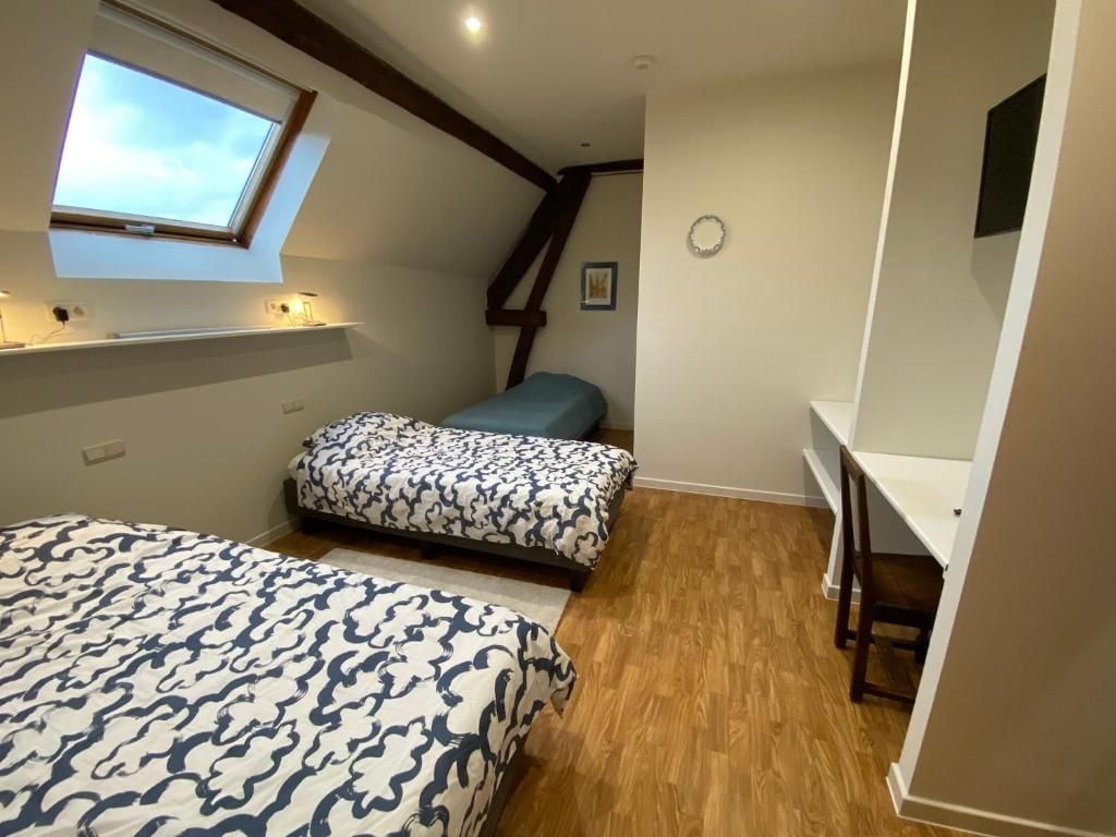 Une chambre avec deux lits, une lucarne, un bureau et un escalier.