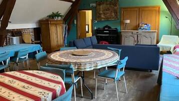 Een eetgedeelte met ronde tafels en blauwe stoelen, een keuken op de achtergrond en houten balken in het plafond.