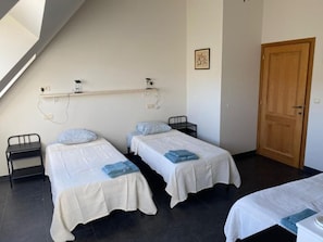 A room with two beds, a wooden door, and a shelf with electrical outlets. - Ferme du Laid Burniat (Chaumont-Gistoux)
