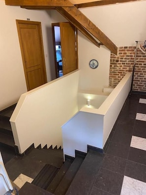 Un escalier avec une rampe blanche et des marches noires, menant à une pièce dont un mur est en briques et qui est ornée d’un motif circulaire bleu.
