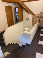 Una escalera con barandilla blanca y peldaños negros, que lleva a una habitación con pared de ladrillo y un adorno circular azul.